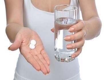 hand with pills medicine tablets and glass of water for headache